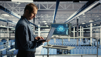 Fototapeta premium Data center technician monitors operational metrics on laptop inside a server room to improve infrastructure performance.