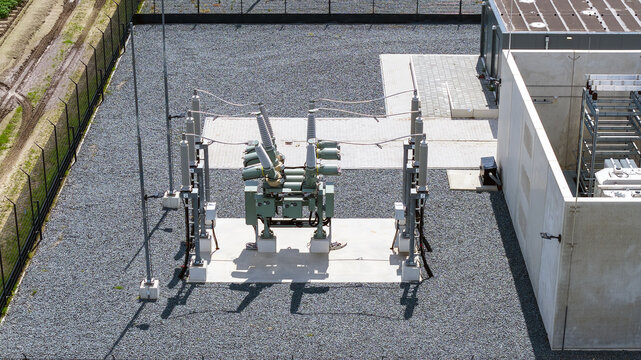 Aerial view of high-voltage electrical substation equipment with circuit breakers on a concrete pad surrounded by gravel in Espel, Flevoland, Netherlands.