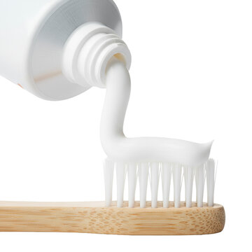 White fluoride toothpaste being squeezed from a minimalist tube onto the transparent bristles of a natural bamboo toothbrush against a transparent background freshness