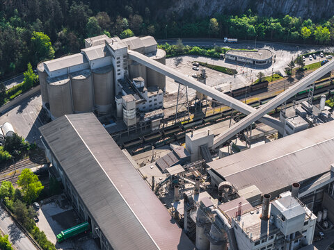 Aerial view of an industrial area featuring large concrete silos, factory buildings, railway tracks with freight trains, and trucks in Prague, Prague, Czechia.