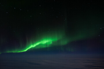 The green Northern Lights Aurora Borealis stretched across the sky above the clouds, as seen from a plane © Richard Waghorn