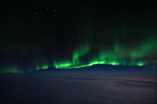 The green Northern Lights Aurora Borealis stretched across the sky above the clouds, as seen from a plane