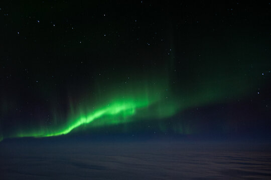 The green Northern Lights Aurora Borealis stretched across the sky above the clouds, as seen from a plane