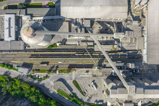 Aerial view of an industrial area with large silos, railway tracks with freight trains, factory buildings, and paved roads in Prague, Prague, Czechia.