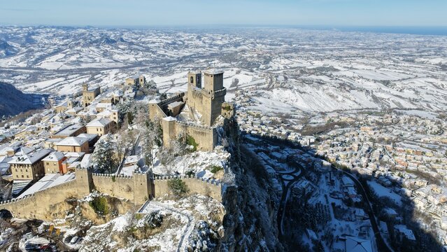 Aerial view of Guaita Tower surrounded by snow-covered historic buildings and stone fortifications on Mount Titano in Citta di San Marino, San Marino, San Marino.