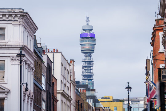 LONDON, UK. 16th  February 2025. A low angle, vertical shot captures the iconic BT Tower rising above a row of classic London brick townhouses and modern buildings under an overcast sky. 