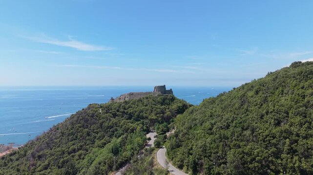 Aerial view of Castello di Arechi on a forested hill above Salerno, Italy, with the Gulf of Salerno, coastal waters and winding mountain road