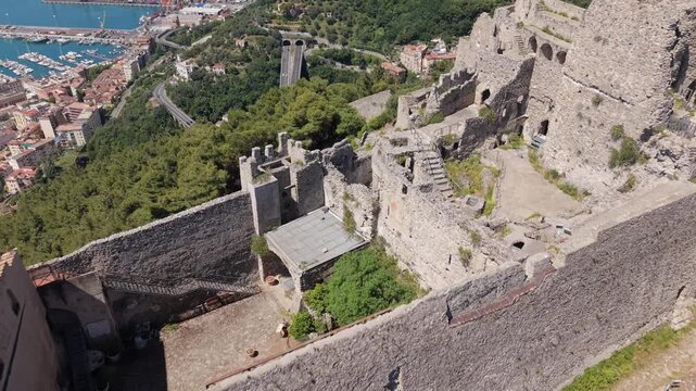 Aerial view of Castello di Arechi stone ruins and ramparts overlooking Salerno container port, marina, and Amalfi Coast mountains, Italy