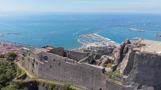 Aerial view of Castello di Arechi imposing stone walls and towers on a forested hilltop overlooking Salerno port and Gulf of Salerno, Italy