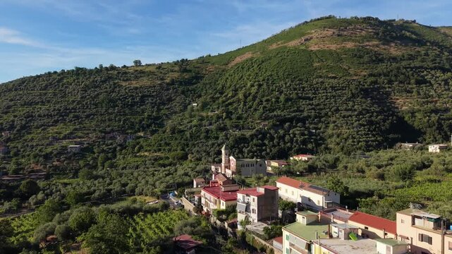 Aerial view of Aurano village with Parrocchia Sant'Agnello Abate church bell tower, rooftops and terraced olive groves on mountain slopes in Gragnano, Naples, Italy
