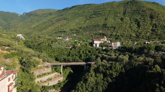 Aerial view of modern road viaduct over green valley with Parrocchia Sant'Agnello Abate church on sunny hillside among lush trees in Aurano, Gragnano, Naples, Italy

