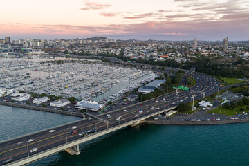 Obraz premium Aerial view of Auckland Harbour Bridge and Viaduct Harbour Marina in Auckland, New Zealand. Cars drive across the bridge during the day.