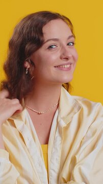 Smiling playful happy young woman blinking eye, looking at camera with toothy smile, winking and flirting, expressing optimism. Excited lady isolated alone on yellow studio background. Lifestyles