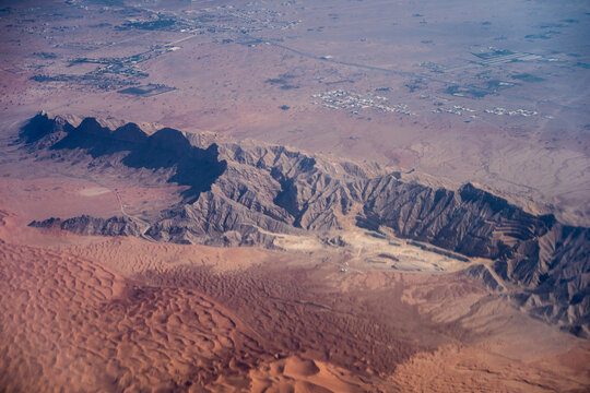Aerial view of a rugged mountain ridge rising from the arid desert landscape with vast sand dunes and dry terrain in Nairobi, Nairobi County, Kenya.