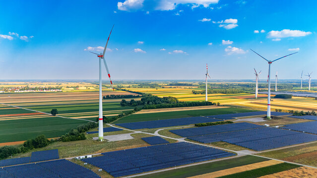 Wind turbines and solar panels in fields. Wind turbines stand tall in fields next to rows of solar panels under a clear sky during daytime.