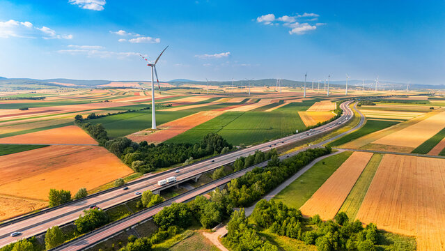 Turbines dot fields by highway. Wind turbines spin in fields near a highway on a sunny day.