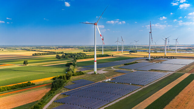 Wind and solar energy sector. Wind turbines and solar panels cover the land. Green fields stretch across the horizon under a blue sky.
