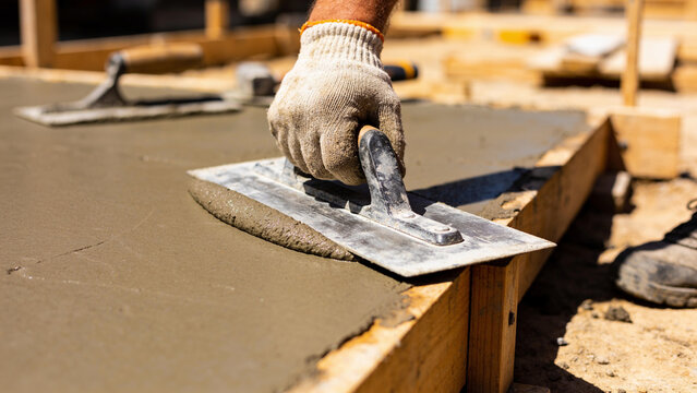 Worker Smoothing Fresh Concrete with Hand Trowel on Construction Site