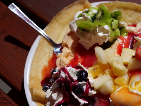  A high-angle, detailed 
close-up shot looking down at a 
luxurious fruit crepe dessert. A silver 
spoon is partially sunk into a scoop of 
vanilla ice cream mixed with red fruit 
syrup. The colorful 
