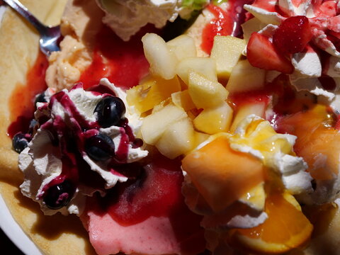  A vibrant, high-angle 
close-up shot showcasing the rich 
variety of toppings on a sweet dessert 
crepe. The view focuses on fresh 
chopped apples, melon pieces, and an 
assortment of berries embedde