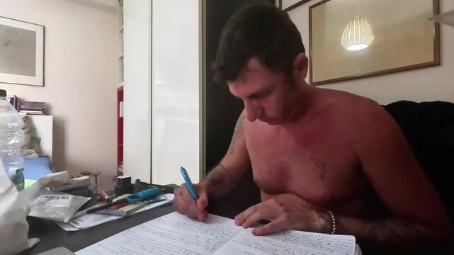 Time-lapse of a man studying sitting at a desk writing notes in a notebook. The man is forty-two years old and bare-chested