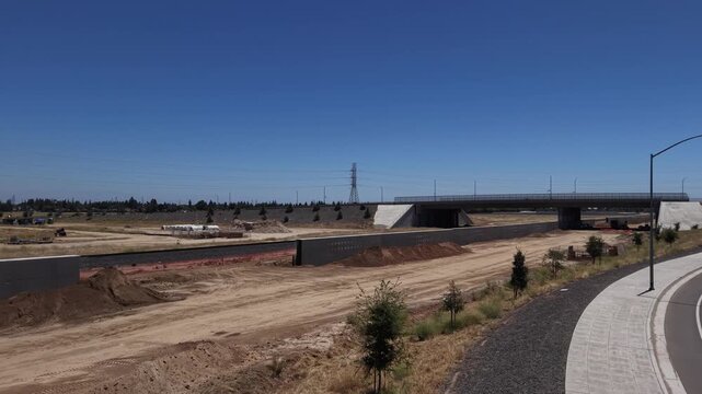 Reversing Aerial Drone Shot Over Construction Area Alongside Road With Overpass Traffic and California High Speed Rail Dirt Piles and Light Pole