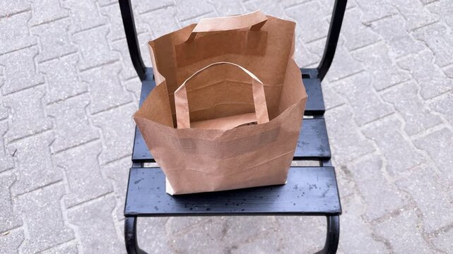 Paper kraft bag for takeout food on a black folding chair, eco-friendly food delivery packaging on a city sidewalk