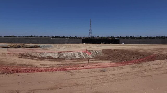 Forward Moving Aerial Drone Shot Toward Excavation Hole With Orange Safety Netting at California High Speed Rail Construction Site With Intrusion Barrier Walls