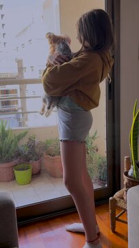 Happy girl hugging her yorkie puppy near the window of her flat.Teenager enjoying a cute moment with her puppy in a sunny day. Free lifestyle concept. Moments of calm and happiness.