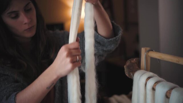 Young Hispanic woman with oiled hands lubricating and shaping wool roving for textile art, showcasing handmade craftsmanship, fiber preparation and creative artisan work.

