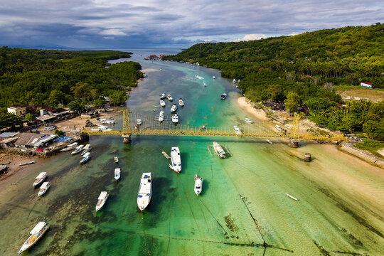 Flying over a yellow suspension bridge spanning a shallow turquoise channel