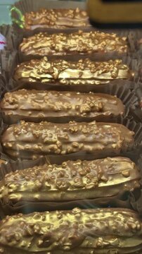 Golden eclairs on display closeup showcasing glossy chocolate glaze and crunchy topping in boutique bakery case, warm ambient