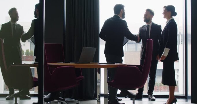 Professional business people meeting in office and working toward successful partnership. Team of three happy people standing in modern office room, exchanging handshakes and clapping hands