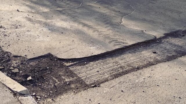 Damaged asphalt curb corner with aggregate, scattered loose asphalt and gravel along cracked pavement next to grassy verge