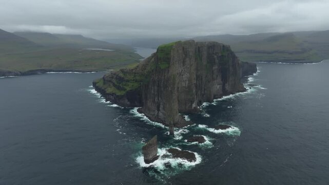 Aerial drone shot pushes in on the dramatic sea cliffs of Ei&eth;iskollur mountain on the Faroe Islands. A remote landscape with rugged coastline and deep blue ocean.