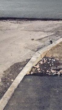 Curb pothole spring highway repair site, empty roadside with cracked pavement and exposed gravel, shallow trench along curb
