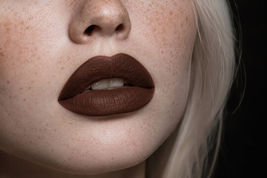 Extreme close up beauty portrait of pale freckled woman wearing matte chocolate brown lipstick, flawless skin texture, luxury makeup, editorial cosmetics concept with dramatic studio lighting