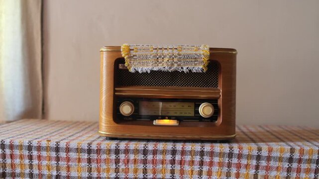 Vintage wooden radio receiver sitting on a plaid tablecloth, showcasing classic design and bringing warm nostalgic feelings with its glowing dial and traditional aesthetic