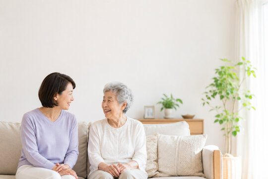 明るいリビングで笑顔で会話する高齢の母親と娘 家族介護・見守り・在宅ケアのイメージ