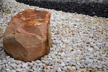 Large sandstone boulder rests on a bed of smooth river pebbles and dark gravel © Thanakrit