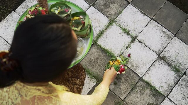 Balinese Woman is performing Traditional Offering Ritual or Worship Ritual at home during Kuningan Ceremony in Bali. Religion, Culture, and Travel Concept. 4K Footage