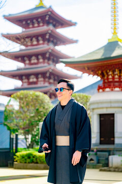 Young smiling Latin man enjoying the moment while holding his smartphone at Sensoji temple in Tokyo Japan, wearing a traditional kimono or yukata, with iconic pagoda and visitors in the background