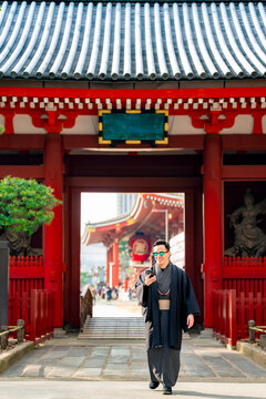 Young smiling Latin man in kimono walks through iconic Sensoji temple gate in Asakusa, capturing blend of traditional Japanese culture and modern urban tourism.
