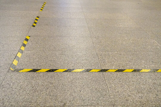Yellow and black hazard tape marking lines on a speckled stone floor