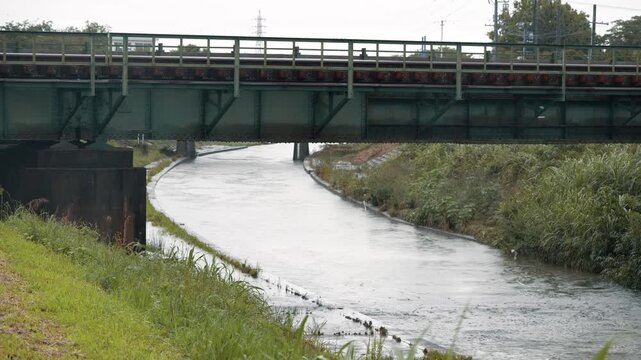 雨が降っている中に川に架かる橋を渡る電車の車両