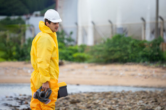 Environmental specialist in protective hazmat suit at industrial site, Worker man wearing yellow protective gear near facility, Safety expert with respirator and tool case at polluted outdoor area