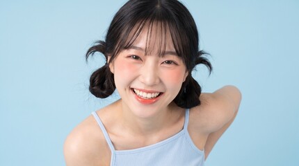 Fototapeta premium Cheerful Young Asian Woman with Twin Bun Hairstyle Smiling Brightly Against a Soft Blue Background