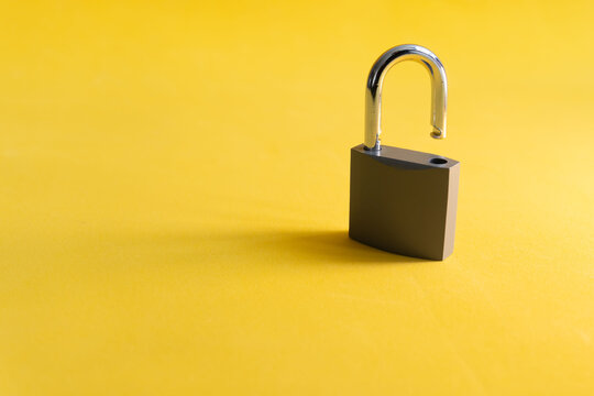 Single metallic padlock stands on bright yellow surface. Its shackle is unlocked, revealing a simple, functional design. Minimalist composition emphasizes isolation and security concepts