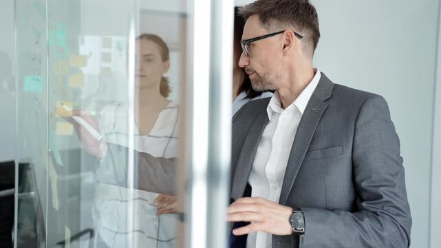 Business team collaborating on strategy, brainstorming ideas with post it notes on a glass board during an office meeting, planning effective project development