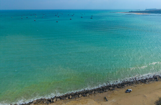 Aerial view of the turquoise waters of the Arabian Sea with numerous small fishing boats anchored offshore and a sandy beach lined with concrete wave breakers in Gwadar, Balochistan, Pakistan.